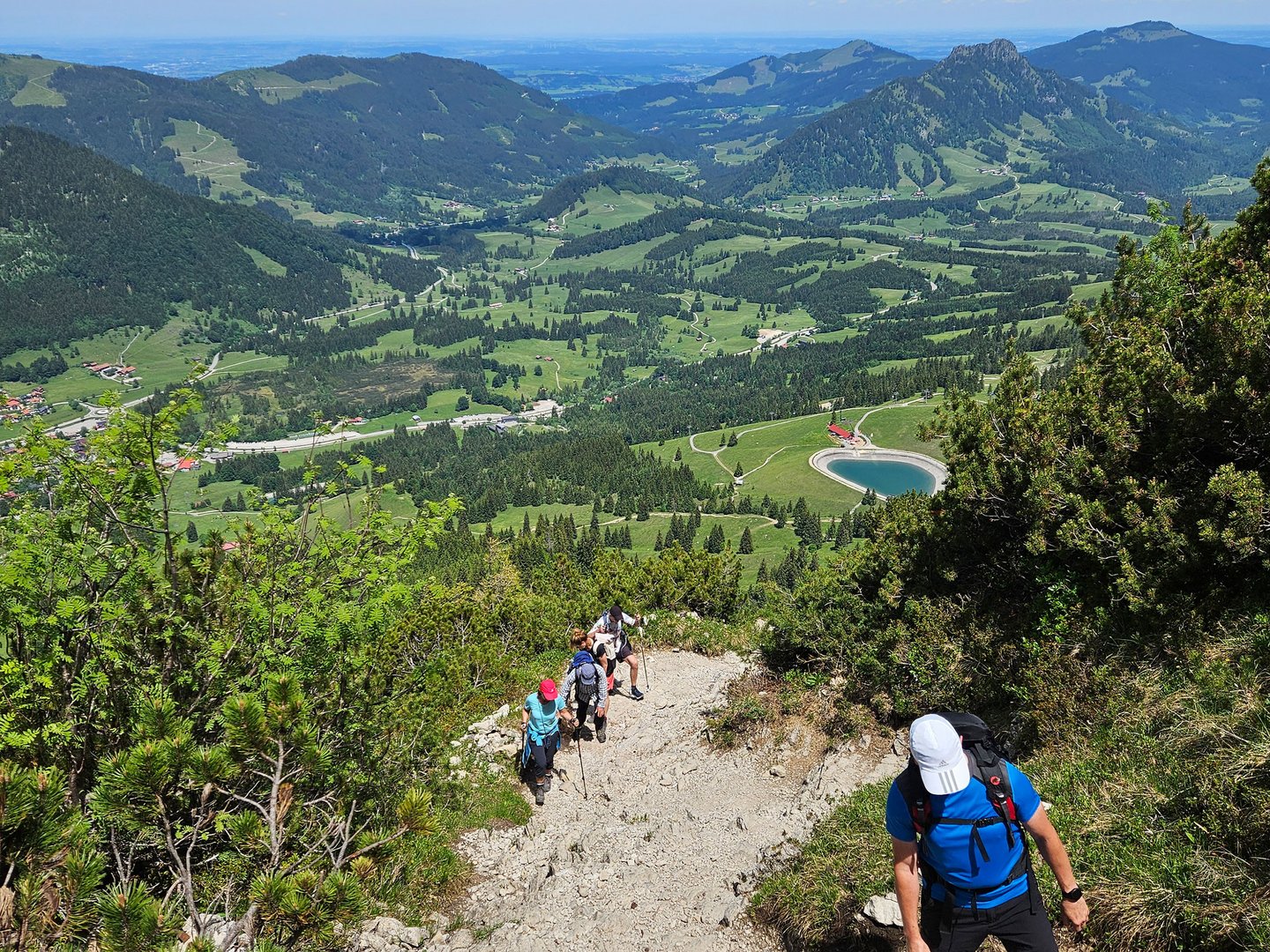 Exklusive Wandertipps von Basti Wanderer steigen auf einem steinigen Bergpfad mit Blick auf grüne Täler und Berge