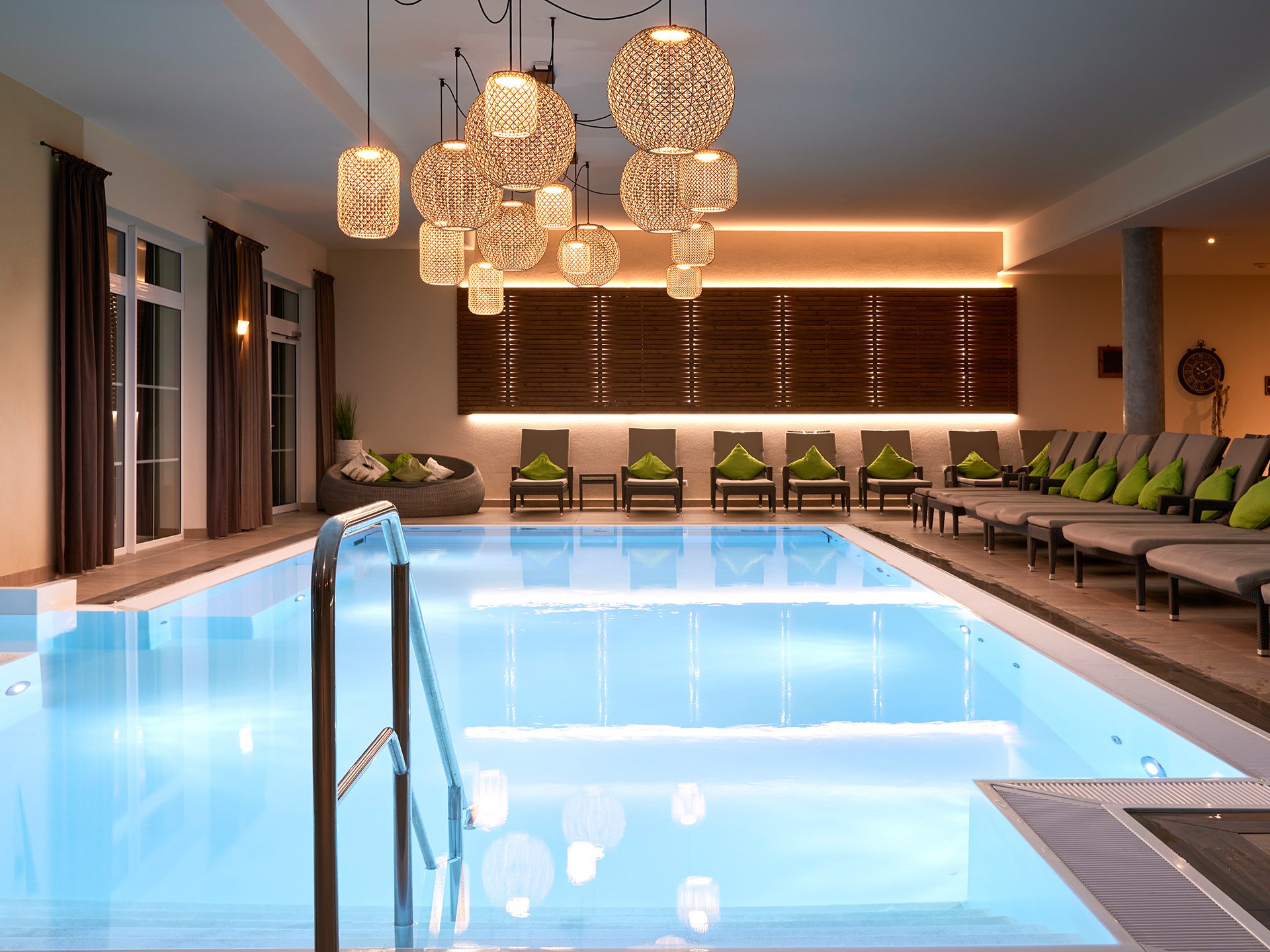 Entspannte Tage im 4*S Panoramahotel Oberjoch! Innenpool mit Liegestühlen und dekorativen Hängelampen in modernem Wellnessbereich