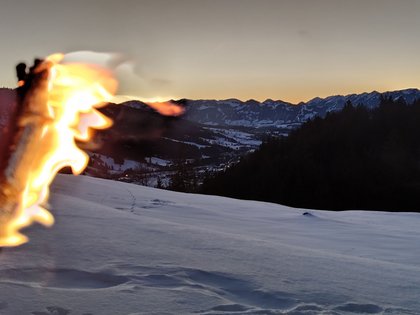 Weihnachtsfeiern im Allgäu Brennende Fackel vor verschneiter Berglandschaft bei Sonnenuntergang