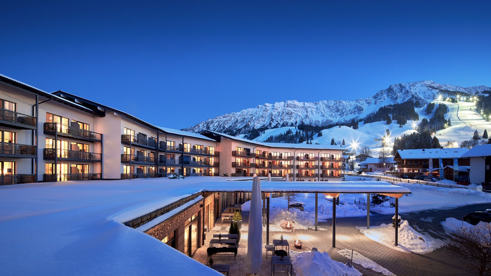 Veranstaltungen im Panoramahotel Oberjoch Hotelgebäude mit beleuchteten Fenstern und verschneiten Bergen im Hintergrund bei Abenddämmerung
