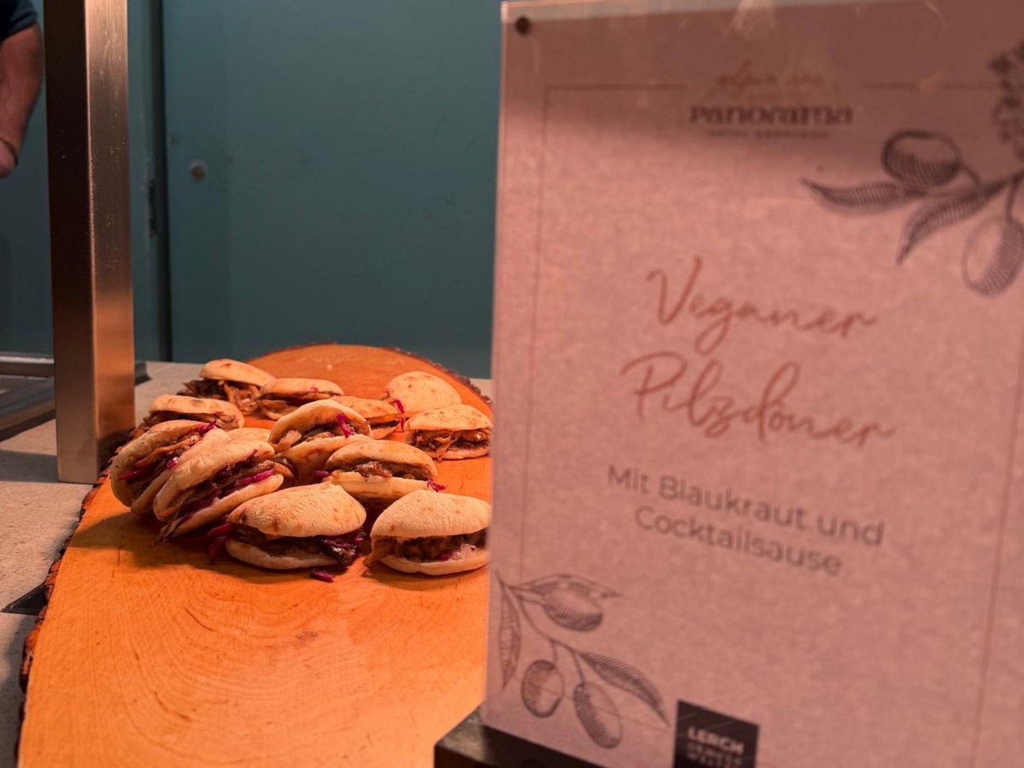 Kulinarikwochen – das Jahresprogramm Vegane Pulled-Sandwiches auf einem Holzbrett neben einem Speisekartenschild